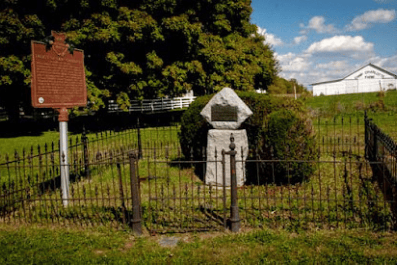 Brown Historical Marker next to gray stone marker surrounded by black iron fence and grass